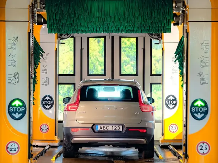 Volvo XC40 i en automatisk biltvätt med autoclean + wax-program. Gröna borstar hänger redo för en skinande ren bil.