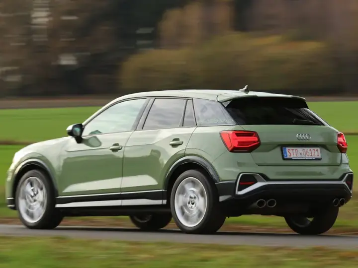 Grön Audi Q2 kör på en landsväg, med suddiga träd och fält i bakgrunden. Kanske ett audi q2 problem med att den kör för fort?