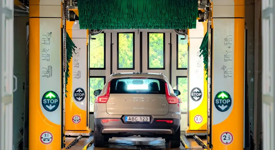 Volvo XC40 i en automatisk biltvätt med autoclean + wax-program. Gröna borstar hänger redo för en skinande ren bil.