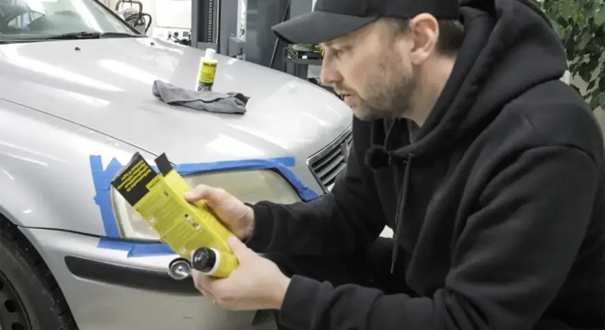 Man förbereder polering strålkastare biltema. En flaska med produkt och trasa ligger på bilen.