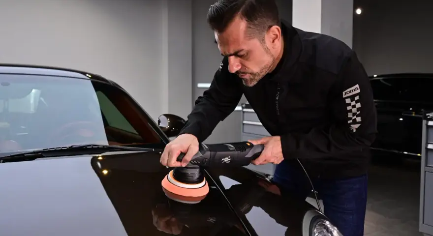 Man polerar en mörk bil med en polermaskin. Autosol ger glans åt lacken.