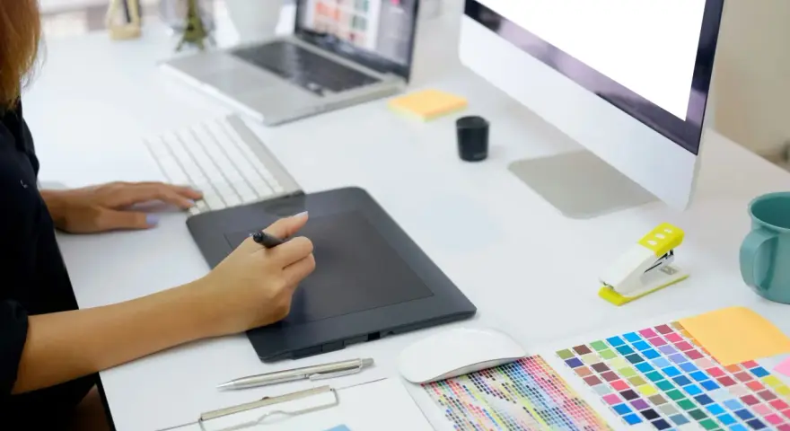 En grafisk designer arbetar vid sitt skrivbord med en ritplatta, tangentbord och en färgkarta. En bra **concept vista prisjakt** för kreativa projekt.