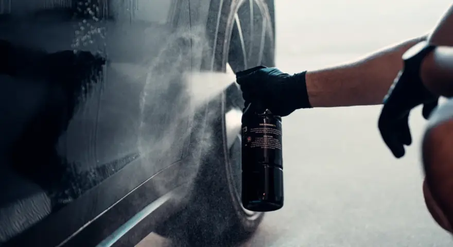 En hand med handske sprayar en bil för att ta bort dekaler.