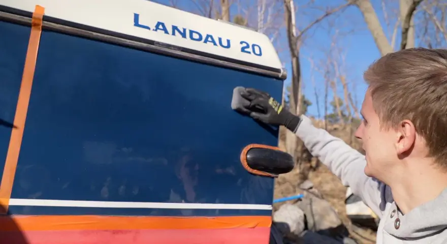 Man applicerar keramisk lackskyddsbehandling på en blå båt med texten "LANDAU 20".