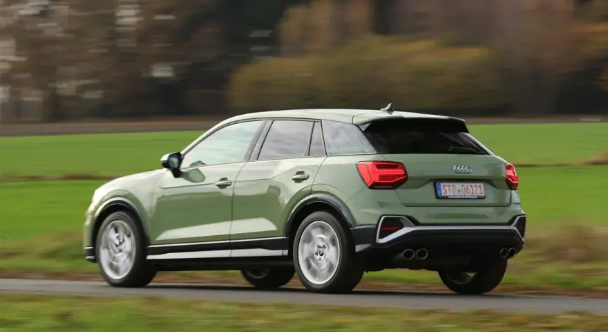 Grön Audi Q2 kör på en landsväg, med suddiga träd och fält i bakgrunden. Kanske ett audi q2 problem med att den kör för fort?