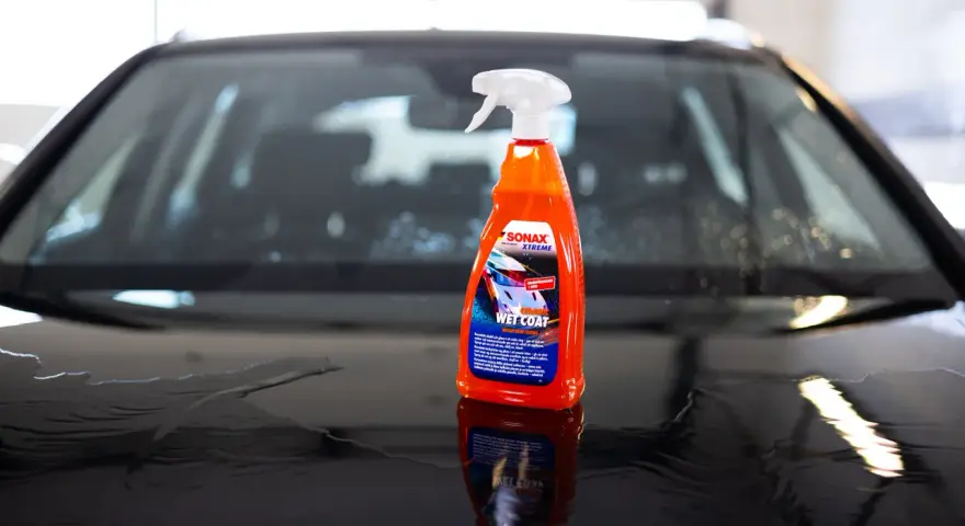 En flaska SONAX Xtreme Ceramic Wet Coat står på en våt bilhuv.