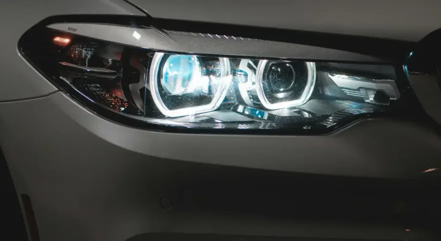 Detaljerad bild av en BMW-bil med tända auto ljus. De blåvita LED-lamporna lyser starkt.