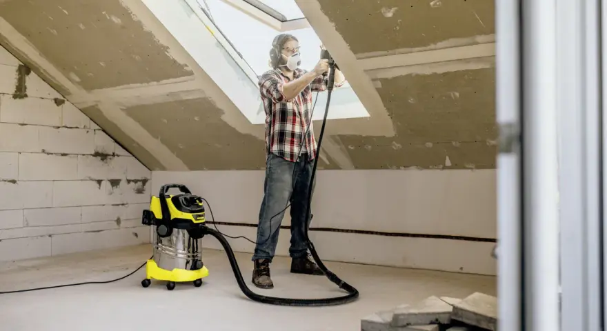 Man med skyddsutrustning använder Kärcher WD 6 för att dammsuga vid renovering av ett vindsrum.