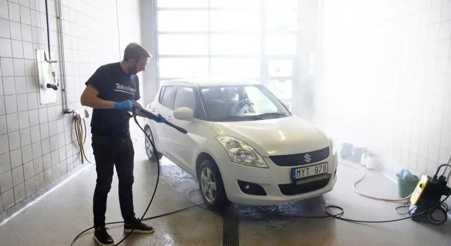 Man med högtryckstvätt gör bilen skinande ren. En riktig asfaltslösare som får bort all smuts.