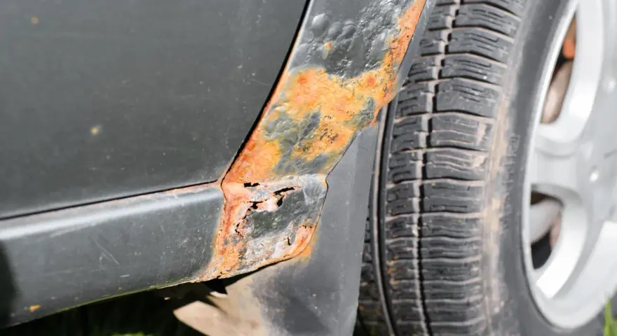 Rostfläckar och skador på bilens skärm nära däcket. En del av lacken har bubblat sig och metallen är synlig. Dags att ta bort repor på bilen och fixa rosten!