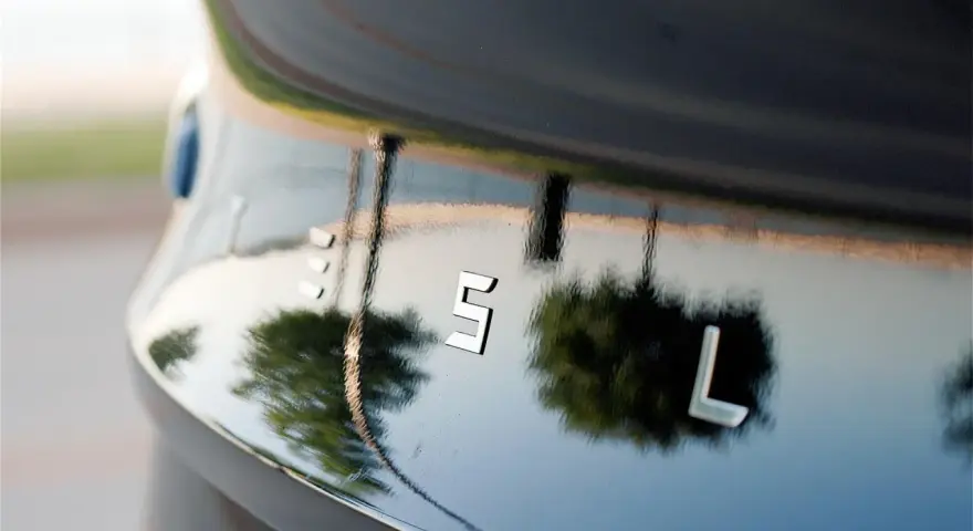 Bilens blanka lack, som en apelsinskal, reflekterar träd och himmel. Bokstäverna "ES L" syns tydligt.