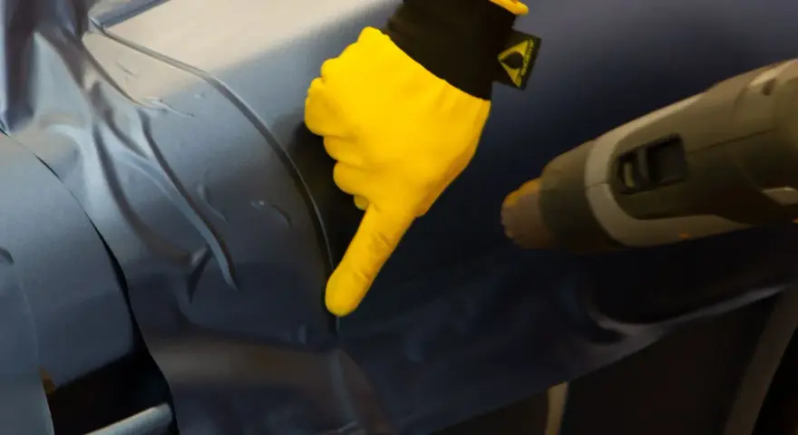 Gul handske pekar på bilens yta där foliering ska tas bort med värmepistol.