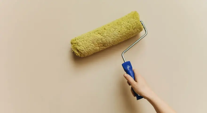 En hand håller en färgroller med gul päls, redo att måla en vägg. Kanske är det dags för en 3m rubbing för att fräscha upp hemmet.