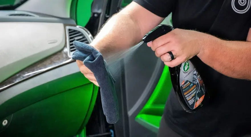 Person sprayar en trasa med en produkt för bilvård, en effektiv wax remover, för att rengöra bilens interiör.