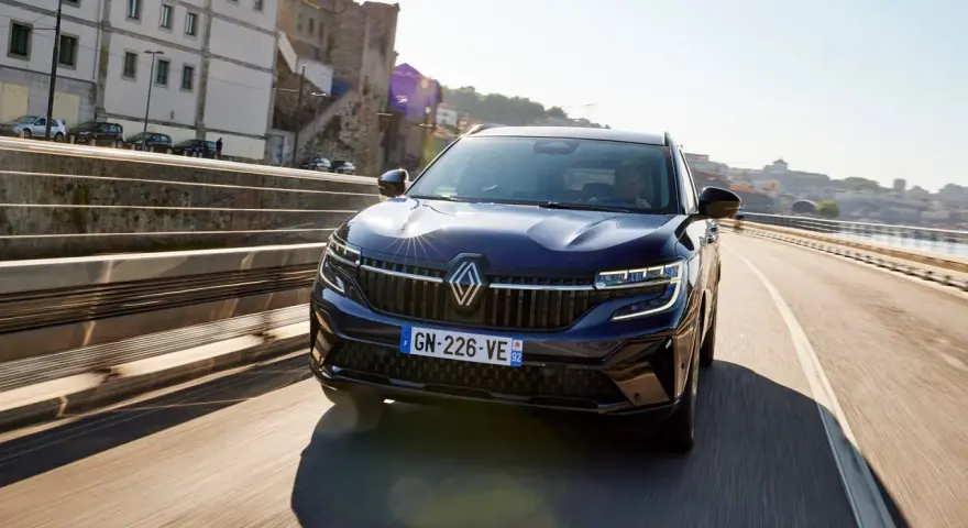 Mörkblå Renault Koleos kör på en bro i solsken. Inga problem syns med bilen.
