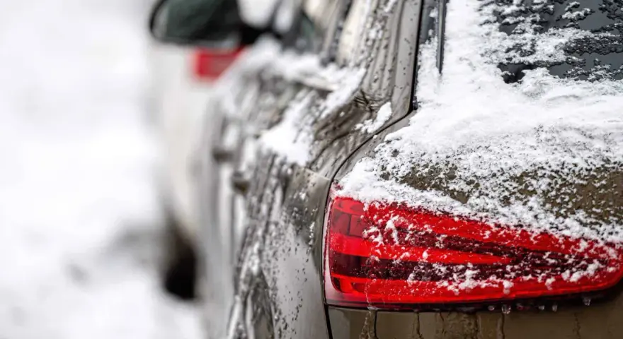 En mörk bil täckt av snö och is. En perfekt dag för ett bilvårdspaket för att få bilen skinande ren igen.
