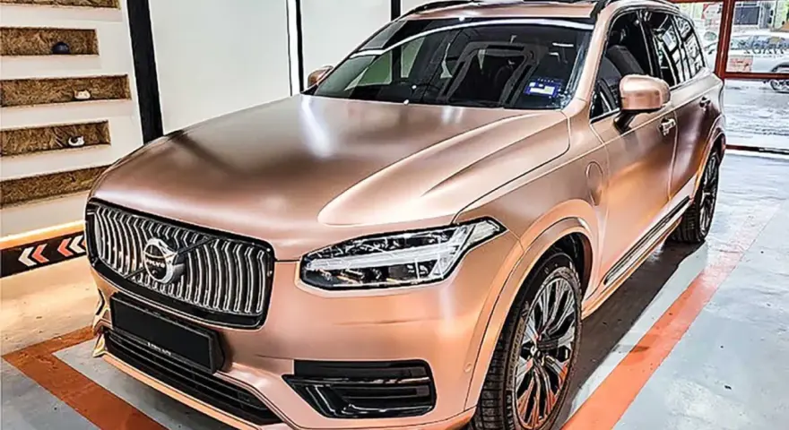 En lyxig Volvo XC90 med en glänsande roséguld folierad bil. Bilen står i ett garage med orange linjer på golvet.