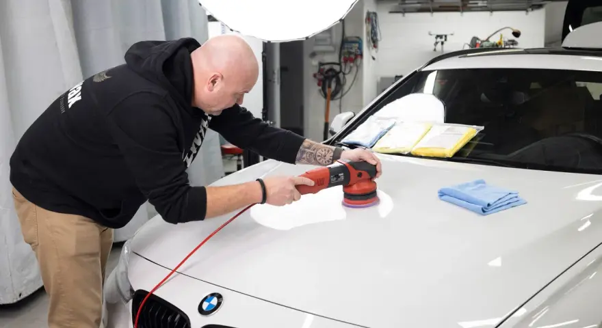 Man polerar en vit bil med en polermaskin, använder Menzerna-produkter för en perfekt finish.
