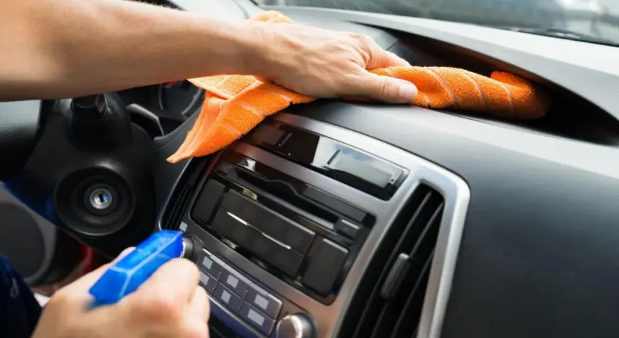 En hand sprayar och torkar av bilens instrumentbräda med en orange trasa. Det ser ut som en magisk rengöring för att få bilen skinande ren.