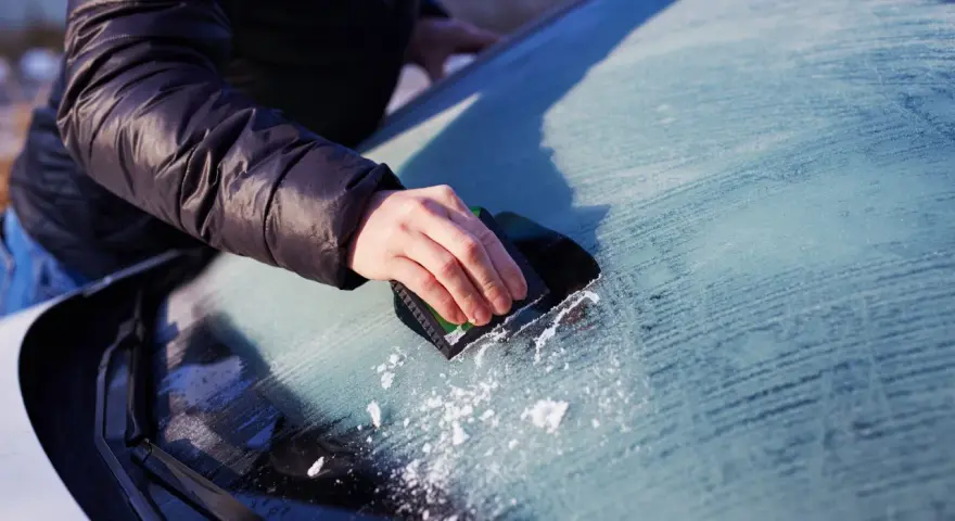 En hand skrapar isfria bilrutor en kall morgon. Snöflingor faller från vindrutan.