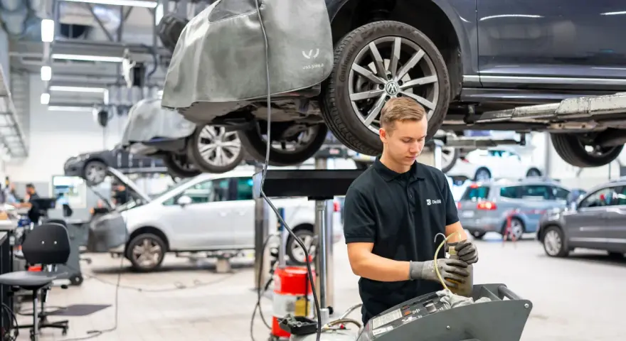 Mekaniker arbetar med en bil på en verkstad. Frågan "hur lång tid tar en bilservice" kan variera beroende på vad som behöver göras.