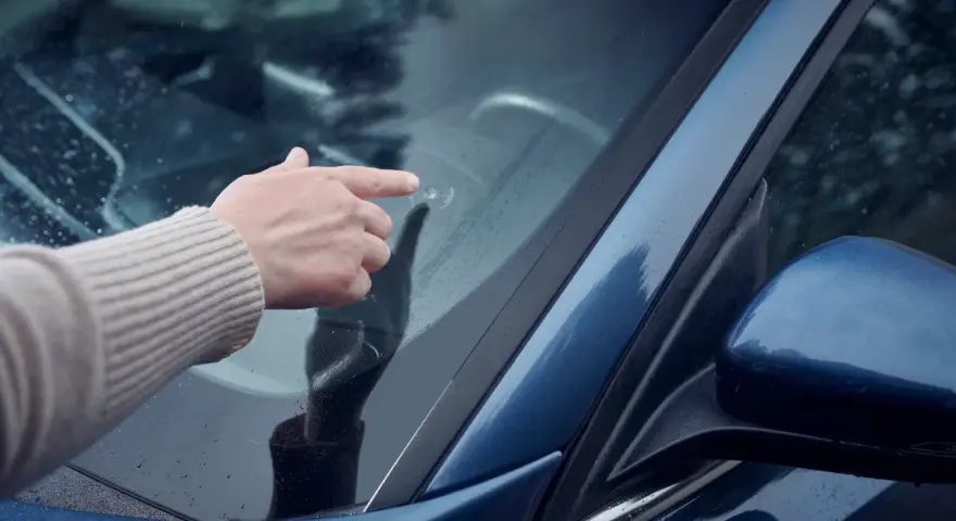 En hand pekar på ett stenskott på vindrutan. En olycklig påminnelse om vägens faror.