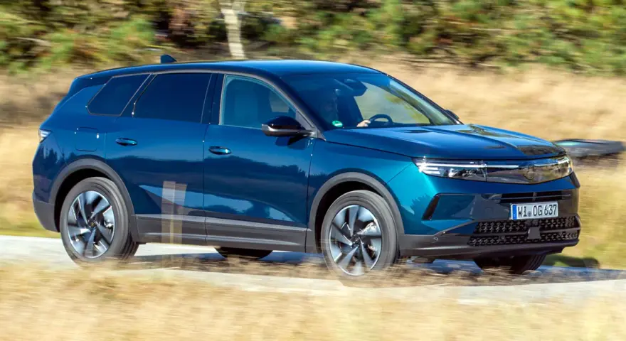 Blå Opel Grandland kör på en grusväg, kanske med ett litet **opel grandland problem** med dammet som virvlar upp.