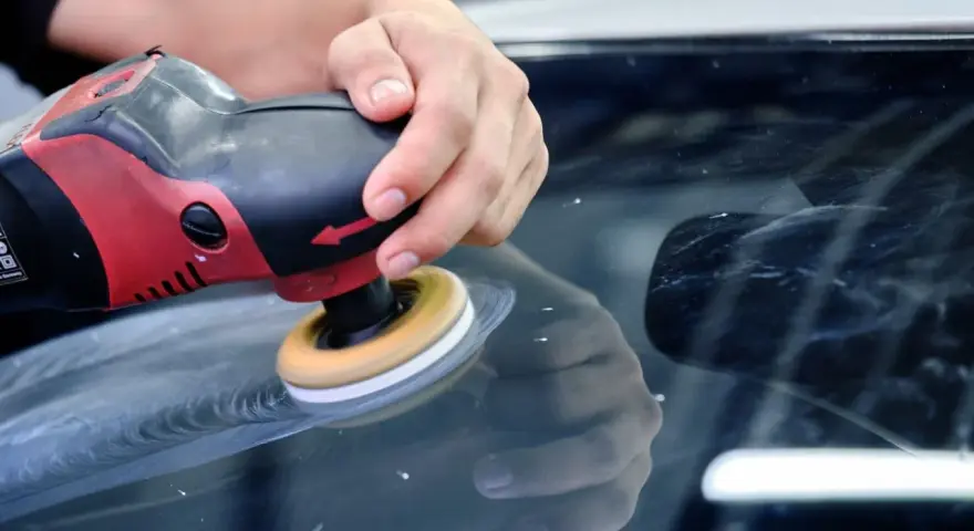 En hand polerar en bilruta med en polermaskin. Glaspolish ger en perfekt finish.
