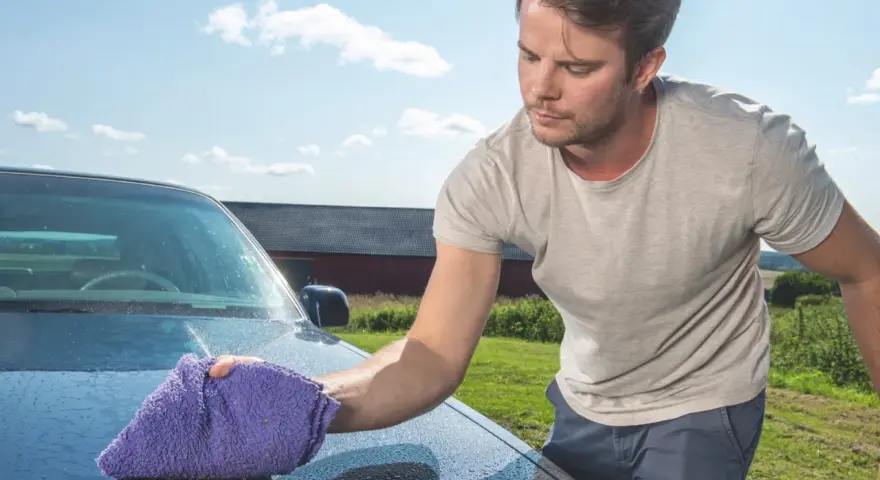Man puts the finishing touches on his car with a waterless wash, leaving a sparkling shine under a blue sky.