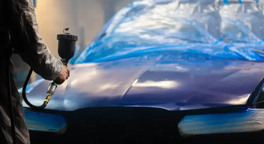 Person lackar om bilen billigt med sprutpistol. Bilen är täckt med blå plast.