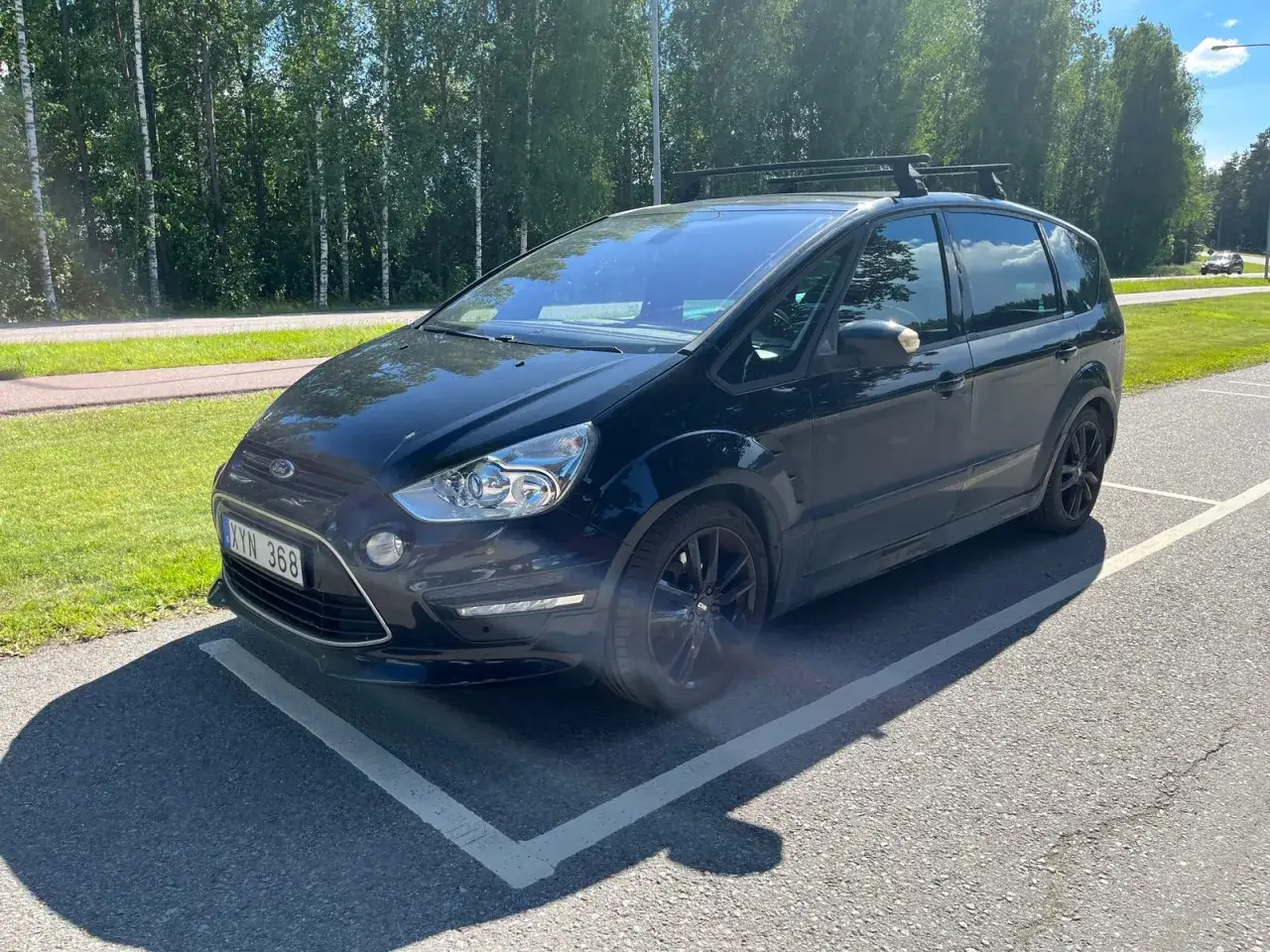 Svart Ford S-Max med takräcke parkerad. En liten skada syns vid främre stötfångaren, ett potentiellt Ford S-Max problem.