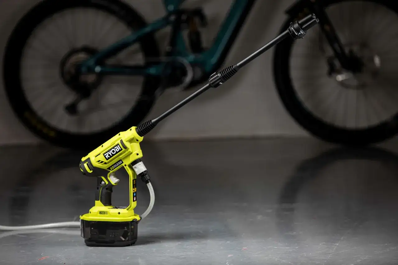 En grön och svart högtryckstvätt från Ryobi, liknande en Kärcher OC3, står redo att rengöra en smutsig cykel.