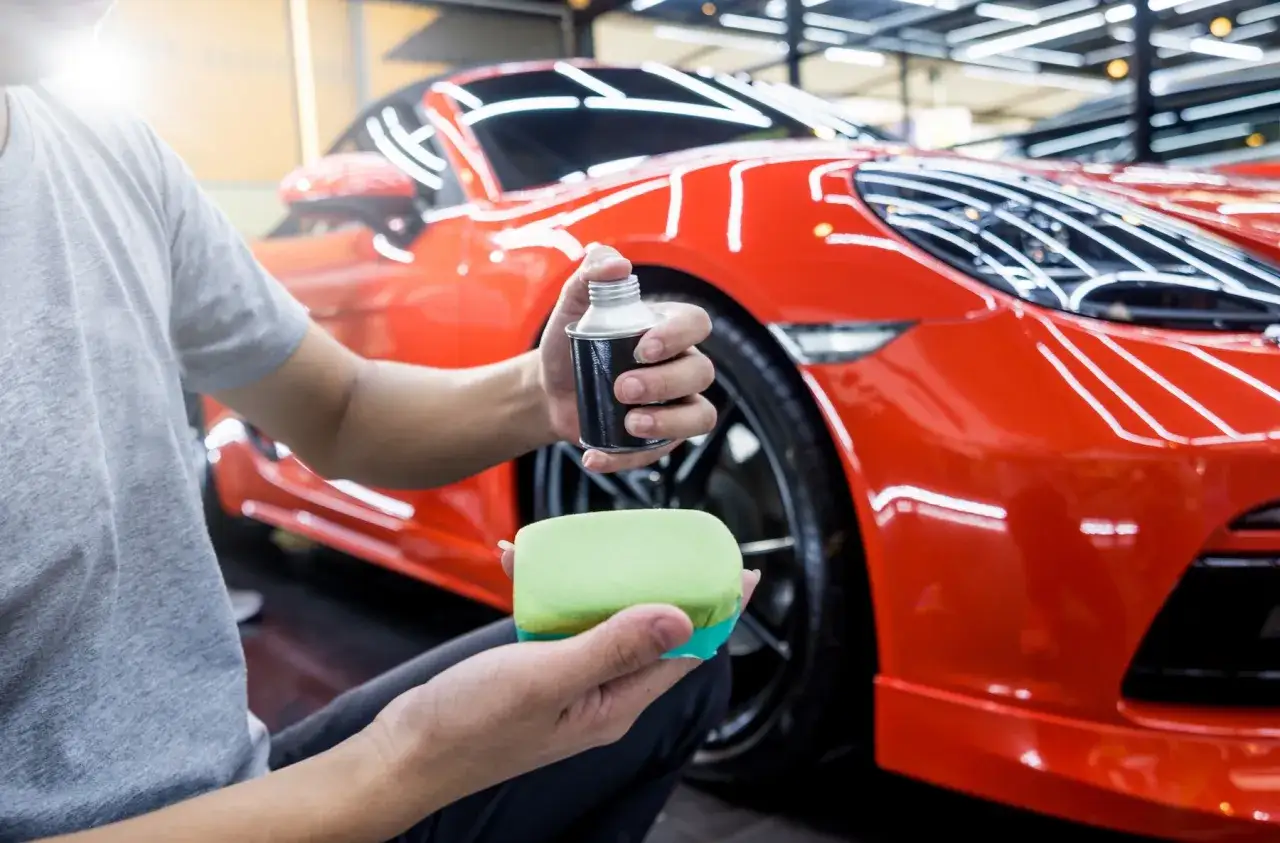 Person applicerar Turtle Wax Pro p&aring; en gr&ouml;n svamp f&ouml;r att polera en skinande r&ouml;d sportbil.