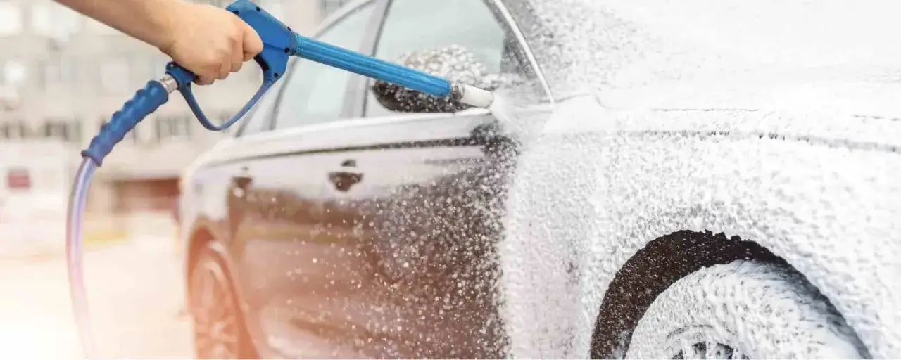 En hand sprutar Autoglym Polar Blast-skum på en bil. Bilen täcks av ett tjockt lager vitt skum.