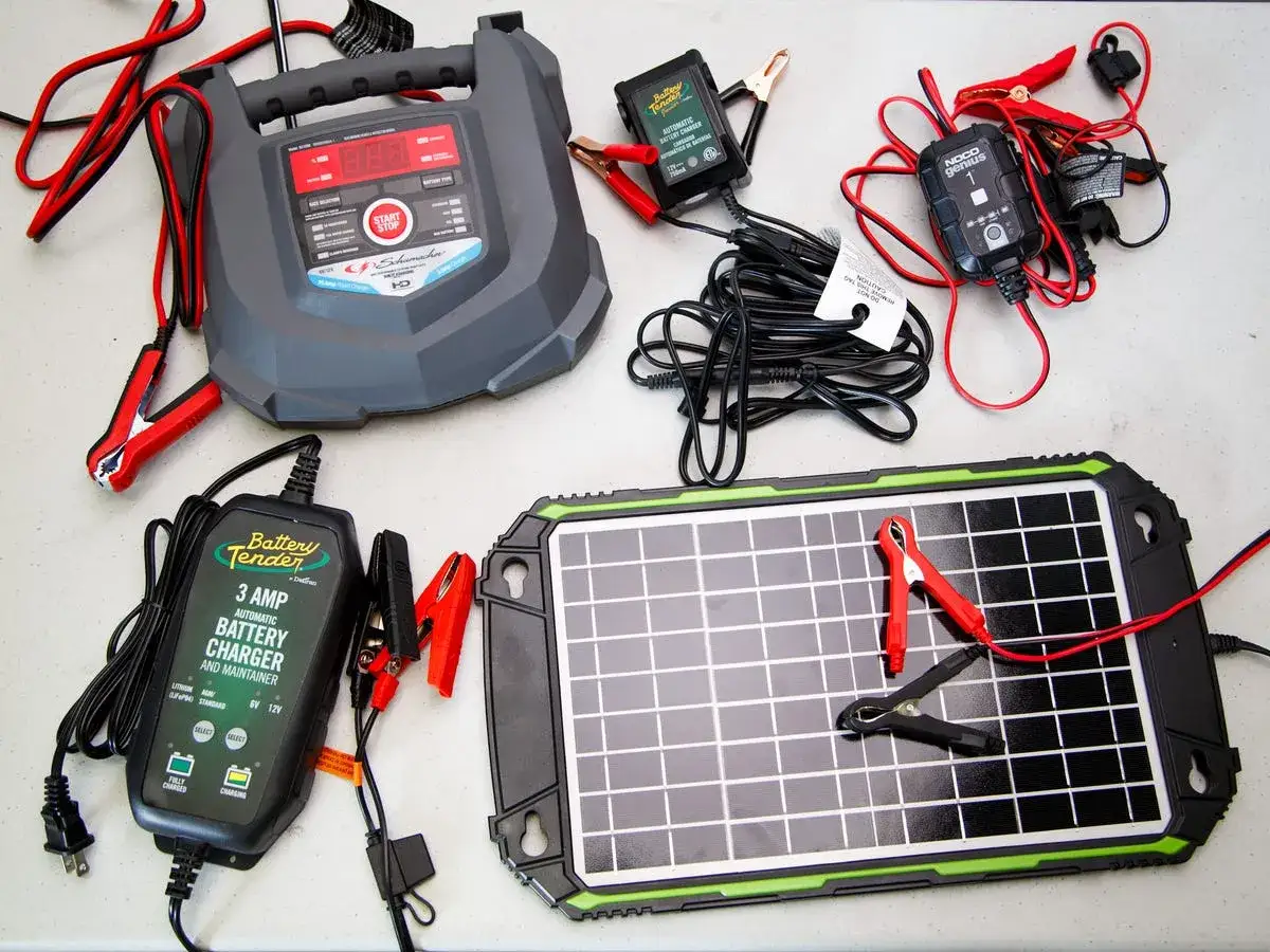 Flera batteriladdare och en solpanel ligger utspridda, redo att ladda bilbatteri.