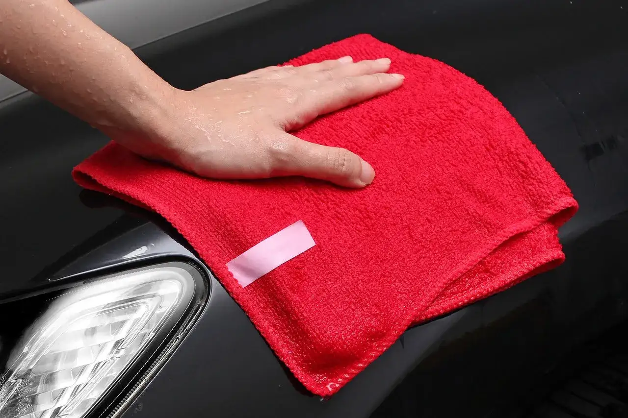 Våt hand torkar en bil med en röd mikrofiberduk, som om den applicerar en hybridvax för glans.