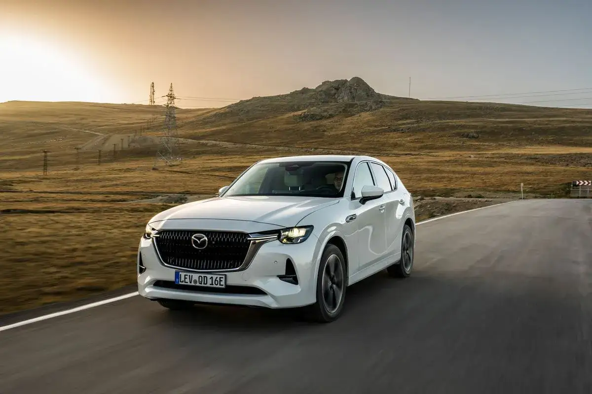 Vit Mazda CX-60 k&ouml;r p&aring; en v&auml;g i ett &ouml;kenlandskap. Kanske &auml;r det en Mazda CX-60 problem med att hitta en laddstation h&auml;r?