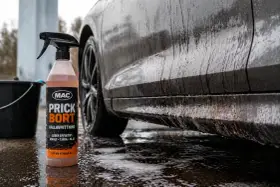 En flaska med MAC Prick Bort kallavfettning står bredvid en smutsig bil. Denna produkt är perfekt för att få bort asfalt, tjära och olja, vilket ger en renare bil.